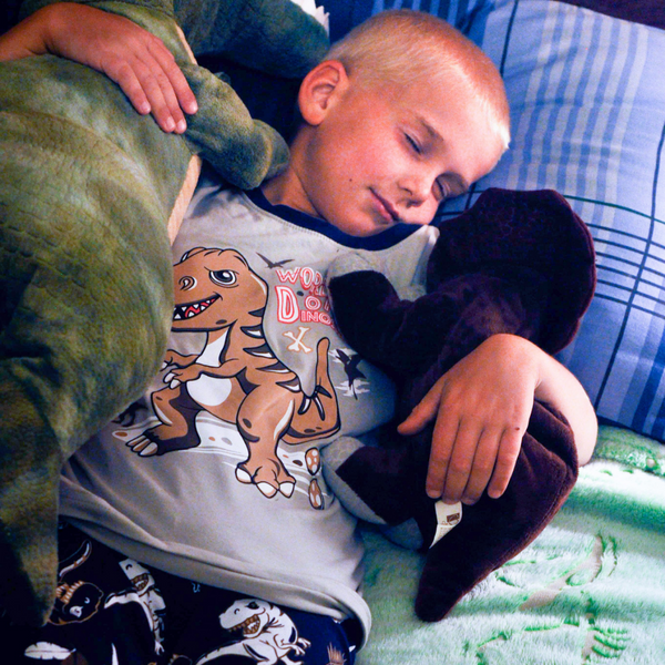 small boy sleeping in t-rex glow in the dark dinosaur pajama set and glow in the dark dinosaur blanket
