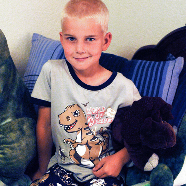 6 year old boy with blonde hair getting ready for bed with the "world of dinosaurs" glow in the dark pajama set on with stuffed dinosaurs